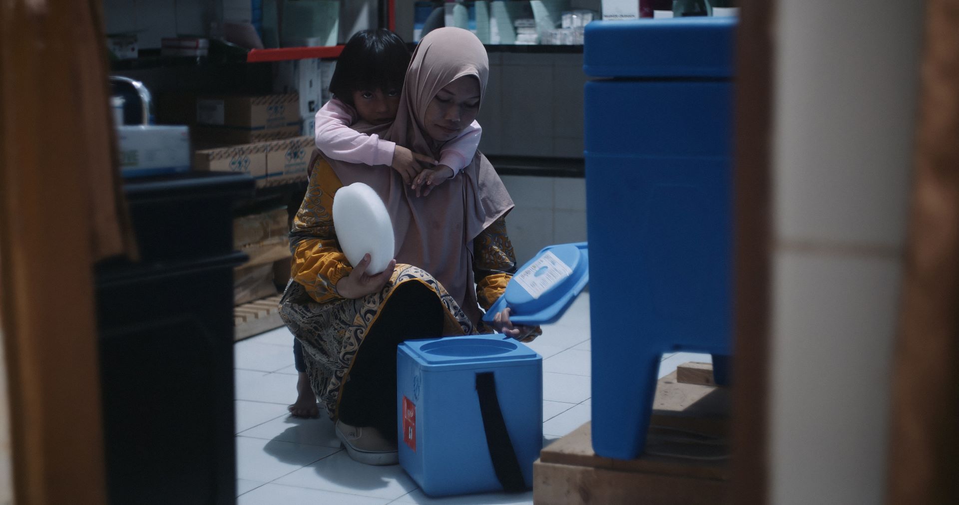Midwife Rahmi (Mimi) prepares vaccines at Baring Primary Health Care Centre in Pangkep, Indonesia, for transport to a remote island, while her daughter watches.